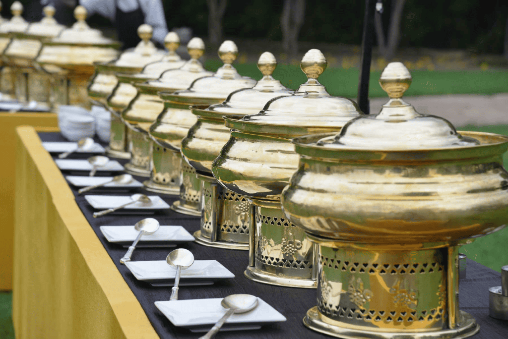 Golden chafing dishes on a banquet table for an outdoor catering event.